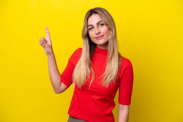 Foto joven uruguaya aislada de fondo amarillo mostrando y levantando un dedo en señal de lo mejor