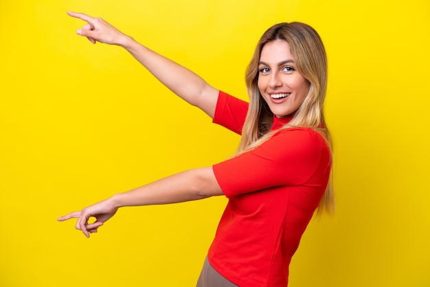 Joven uruguaya aislada de fondo amarillo señalando con el dedo a un lado y presentando un producto