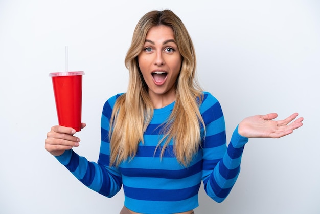 Joven uruguaya bebiendo soda aislada de fondo blanco con expresión facial impactada