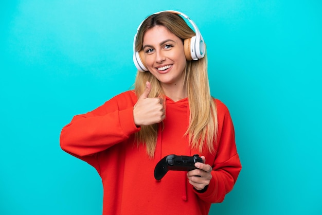 Joven uruguaya jugando con un controlador de videojuegos aislado en azul dando un gesto de aprobación