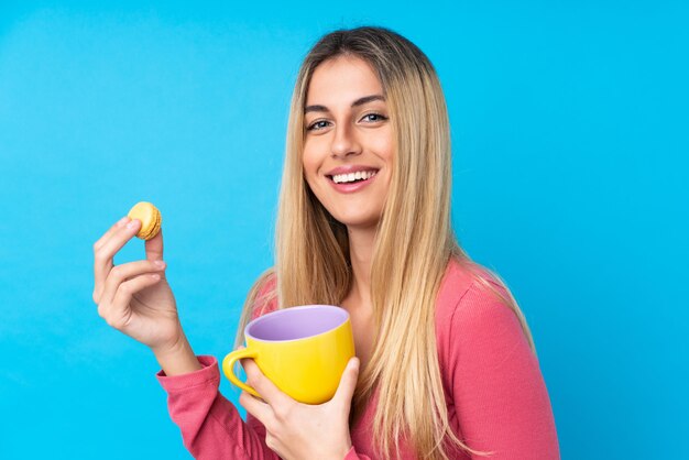 Joven uruguaya sobre pared azul aislada con coloridos macarons franceses y una taza de leche