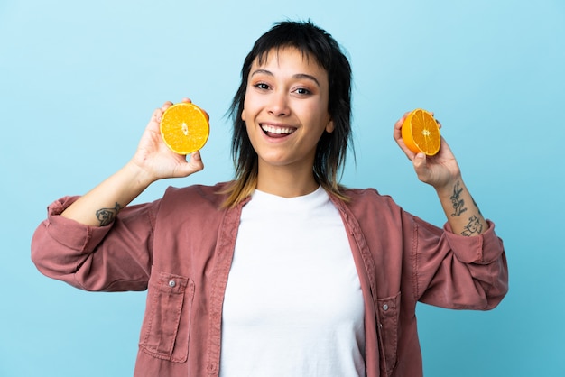 Joven uruguaya sobre pared azul aislada sosteniendo una naranja