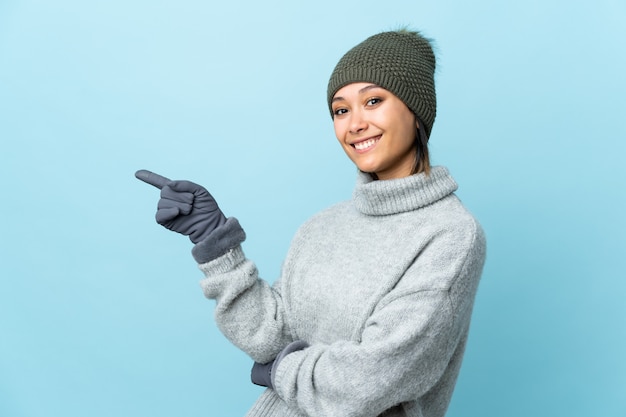 Joven uruguaya con sombrero de invierno en la pared azul que señala el dedo hacia un lado