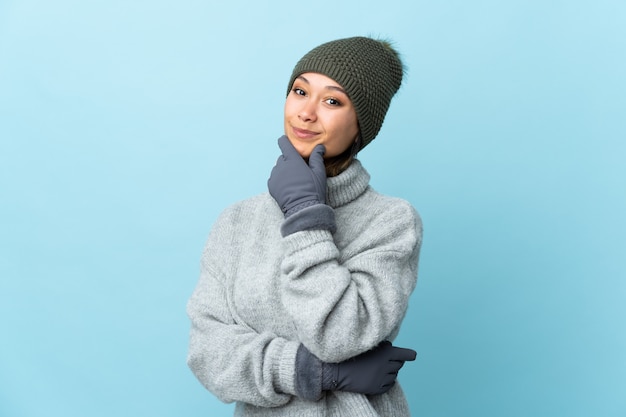 Joven uruguaya con sombrero de invierno en la pared azul riendo