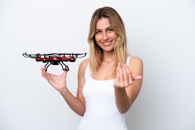 Joven uruguaya sosteniendo un dron aislado de fondo blanco invitando a venir con la mano Feliz de que hayas venido