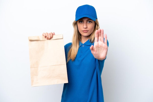 Joven uruguaya tomando una bolsa de comida para llevar aislada de fondo blanco haciendo un gesto de parada