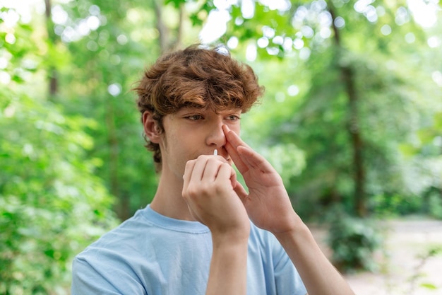 Joven usa aerosol nasal debido a problemas con la nariz y la respiración en el parque público