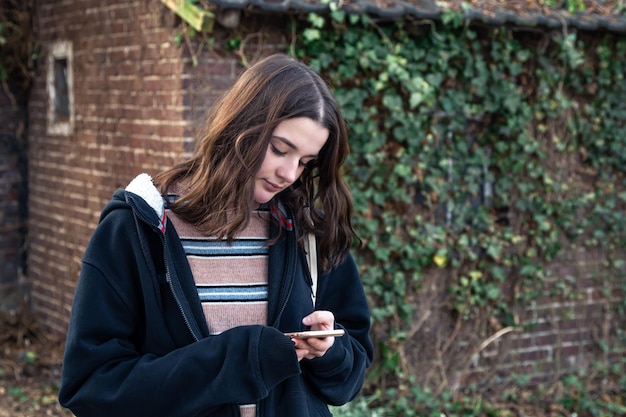 Una joven usa un teléfono en el fondo de una pared con hiedra.