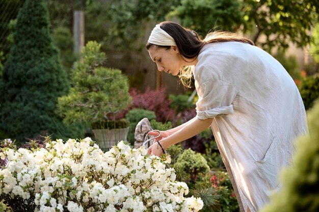 Una joven usa tijeras para decorar el arbusto de flores en un jardín bonsái