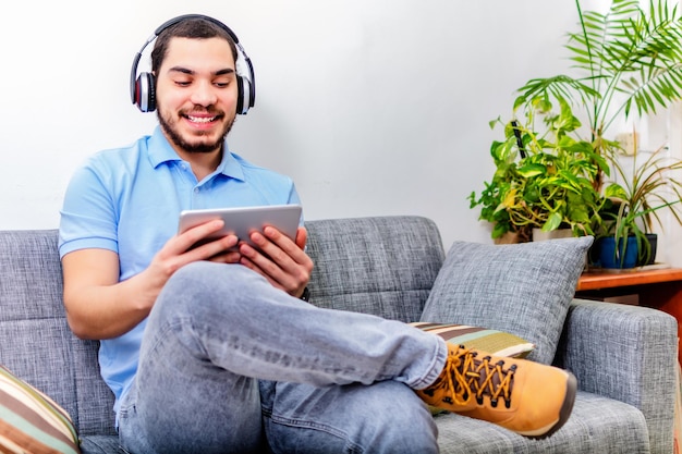 Foto joven usando audífonos usando una tableta elearning en una sala de estar en casa