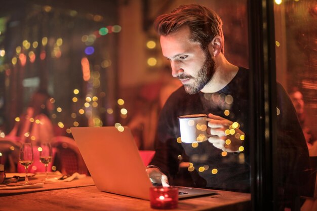 Joven usando una computadora portátil en el escritorio en un restaurante por la noche