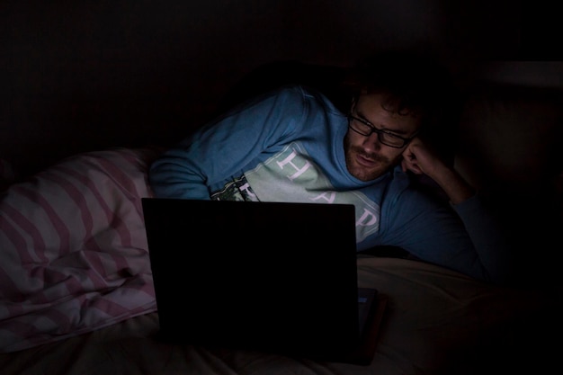 Un joven usando una computadora portátil mientras está acostado en la cama en casa