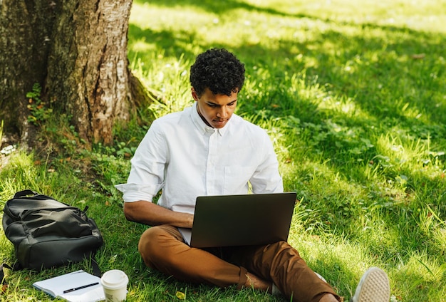 Joven usando una computadora portátil mientras está sentado en el parque