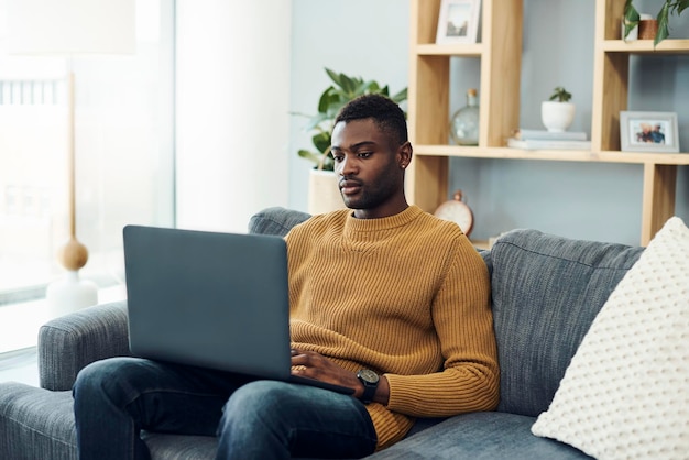 Joven usando una computadora portátil mientras está sentado en el sofá en casa