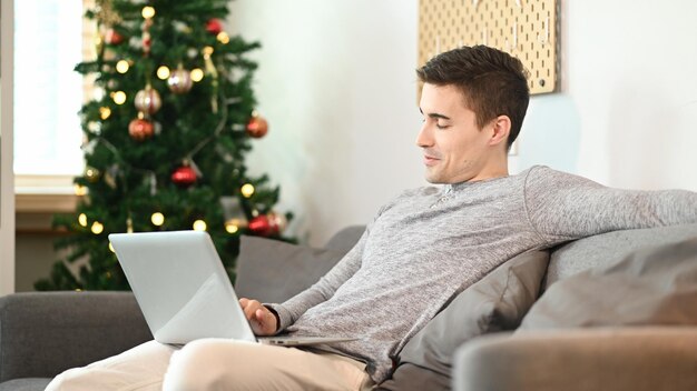 Joven usando una computadora portátil mientras se relaja en un cómodo sofá en casa