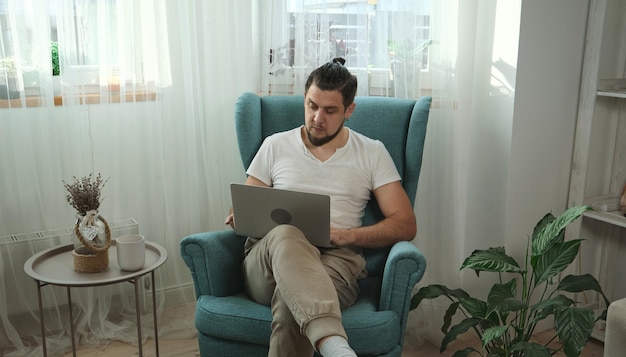 Joven usando laptop escribiendo y trabajando sentado en el sillón en casa