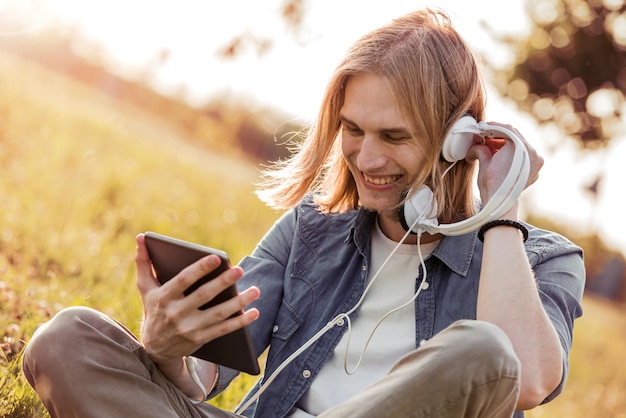 Joven usando tableta en el parque con auriculares