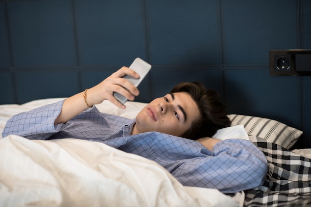 Joven usando teléfono inteligente acostado en la cama