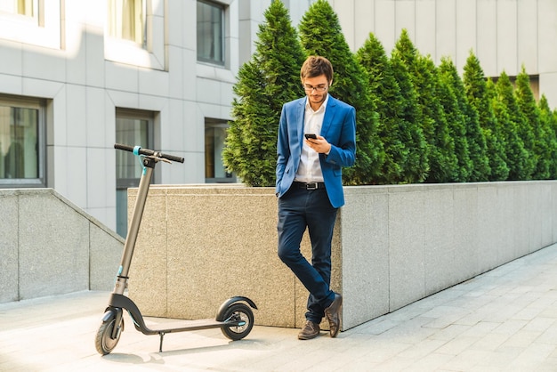 Joven usando teléfono inteligente con scooter eléctrico en la calle de la ciudad Concepto de transporte moderno y ecológico