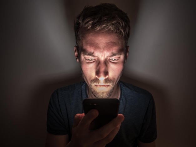 Foto joven usando el teléfono mientras está sentado en el cuarto oscuro