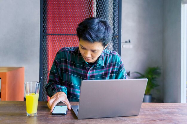 Joven usando teléfono móvil y computadora portátil en el restaurante