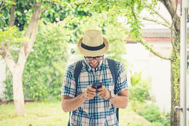 Joven usando el teléfono móvil mientras está de pie contra las plantas