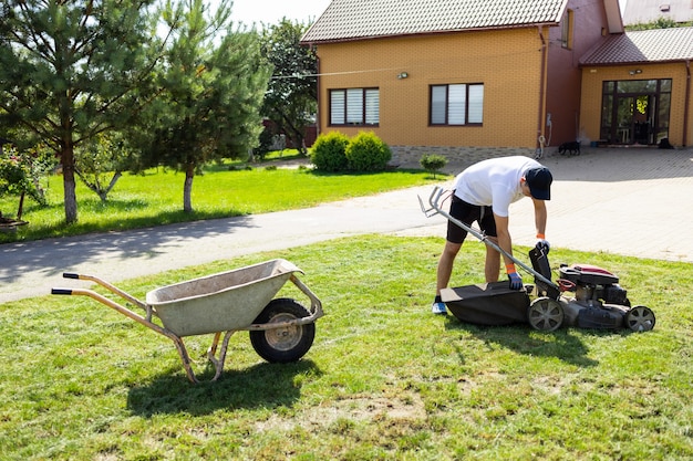 Joven vaciando el recogedor de césped de la cortadora de césped