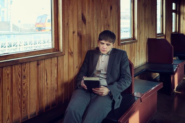 Un joven en un vagón de tren antiguo está sentado leyendo un libro y mirando por la ventana