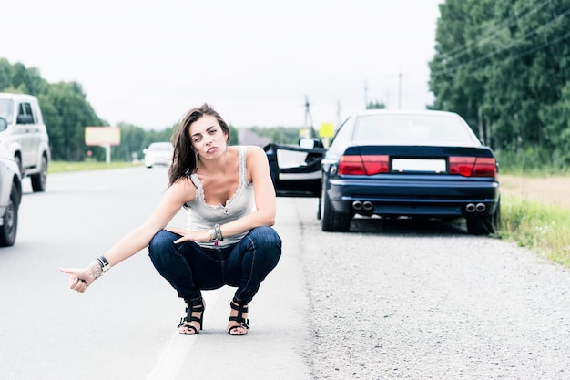 Foto una joven en vaqueros y una camiseta intenta detener el coche para pedir ayuda en la carretera