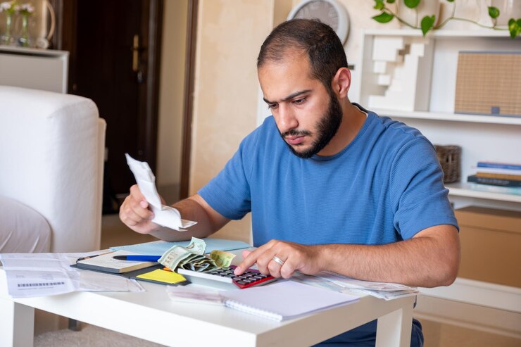 Foto joven varón barbudo calculando el costo de la vida en la sala de estar