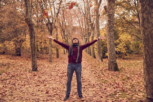 Joven varón blanco caucásico mirando hacia arriba arrojando hojas de árboles en un corredor de árboles Colores de otoño