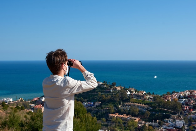 Un joven varón caucásico mirando una vista al mar con binoculares