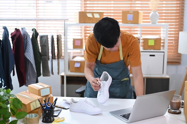 Joven vendedor en línea revisando la orden de compra del producto en una computadora portátil y preparando el paquete para entregarlo al cliente