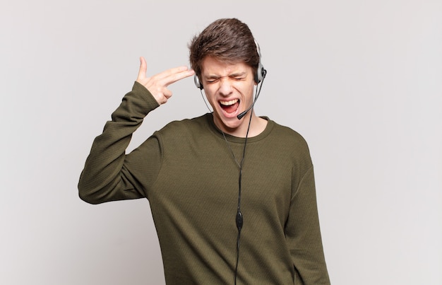 Foto joven vendedor telefónico que parece infeliz y estresado, gesto de suicidio haciendo un signo de pistola con la mano, apuntando a la cabeza