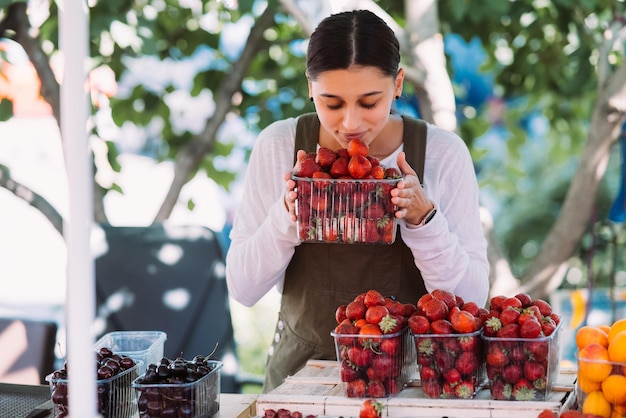 Joven vendedora positiva en el trabajo sosteniendo fresas en sus manos