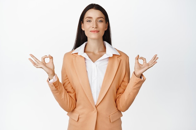 Una joven vendedora que muestra un gesto de nirvana zen meditando practica yoga y se ve tranquila y relajada de pie contra el fondo blanco