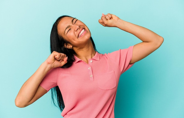 Joven venezolana aislada de fondo azul celebrando un día especial salta y levanta los brazos con energía