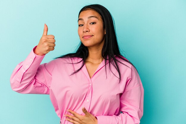 Joven venezolana aislada de fondo azul toca sonrisas de barriga comiendo suavemente y concepto de satisfacción