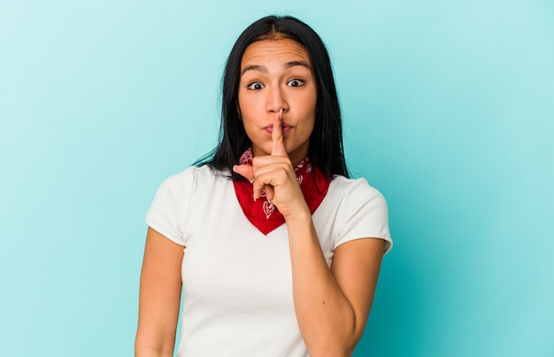 Joven venezolana aislada en la pared azul guardando un secreto o pidiendo silencio.