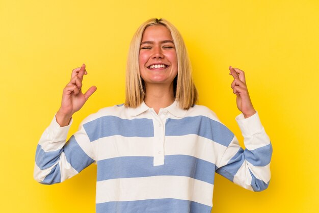 Joven venezolana aislada sobre fondo amarillo cruzando los dedos para tener suerte