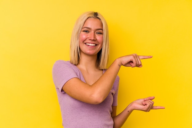 Joven venezolana aislada sobre fondo amarillo sosteniendo algo poco con los dedos índices, sonriente y confiado.