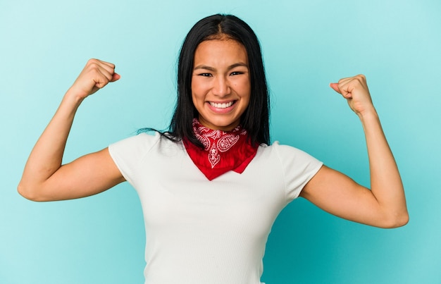 Joven venezolana aislada sobre fondo azul mostrando gesto de fuerza con los brazos, símbolo del poder femenino