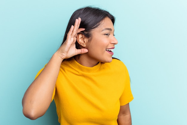 Joven venezolana aislada sobre fondo azul tratando de escuchar un chisme.