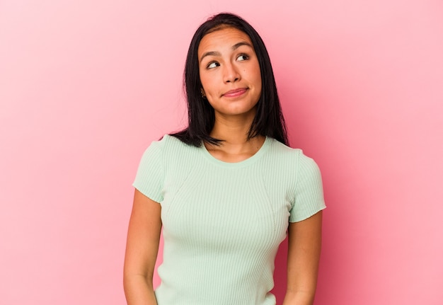 Joven venezolana aislada sobre fondo rosa relajado y feliz riendo, cuello estirado mostrando los dientes.