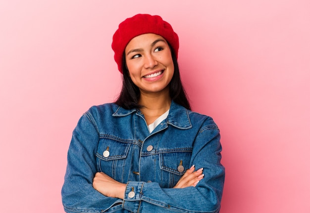 Joven venezolana aislada sobre fondo rosa sonriendo confiada con los brazos cruzados.