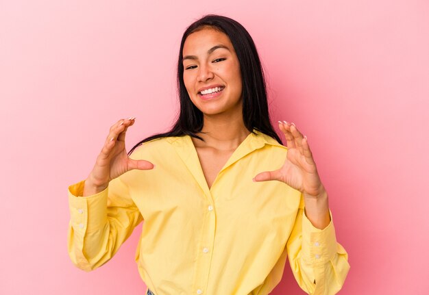 Joven venezolana aislada sobre fondo rosa sosteniendo algo con palmas, ofreciendo a la cámara.