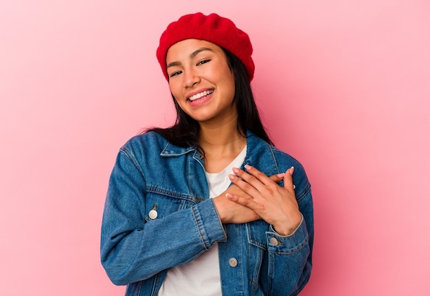 La joven venezolana aislada sobre fondo rosa tiene una expresión amistosa, presionando la palma contra el pecho. Concepto de amor.