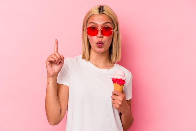 Joven venezolana comiendo un helado aislado en la pared rosa con una gran idea, concepto de creatividad.