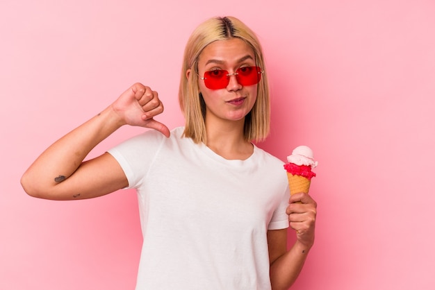 Joven venezolana comiendo un helado aislado sobre fondo rosa se siente orgullosa y segura de sí misma, ejemplo a seguir.