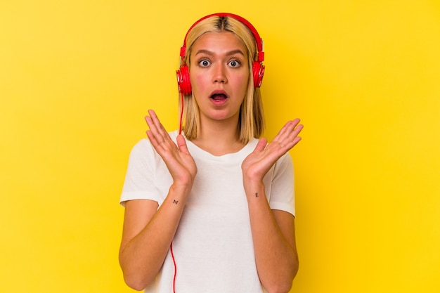 Joven venezolana escuchando música aislada en la pared amarilla sorprendida y conmocionada